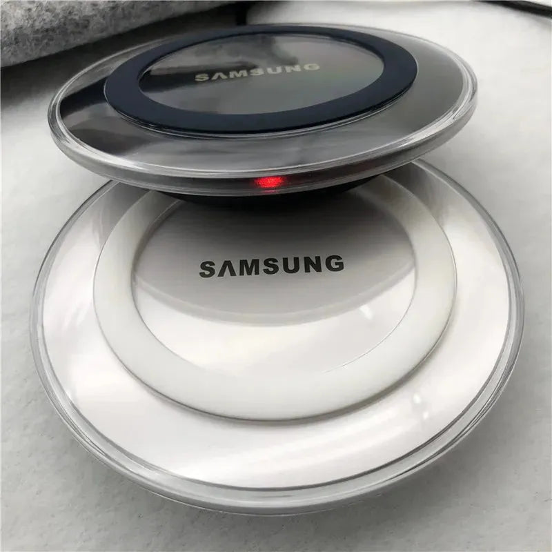 Stacked Samsung Qi wireless charging pads: a dark grey one with a red LED, and a white one. Both round with clear plastic edges.
