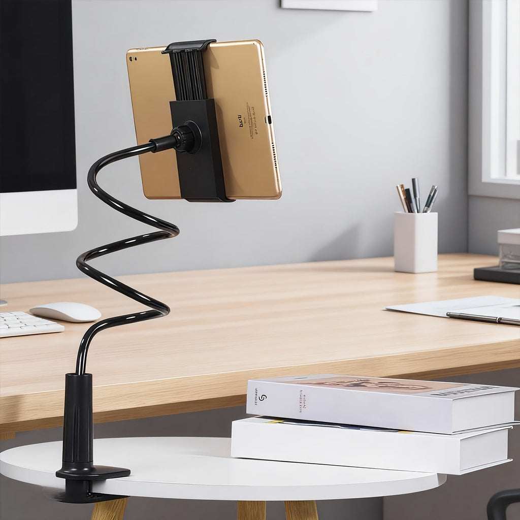 Black flexible gooseneck tablet holder with a gold tablet, clamp-type base on a white table. 360° adjustable for phones and tablets.